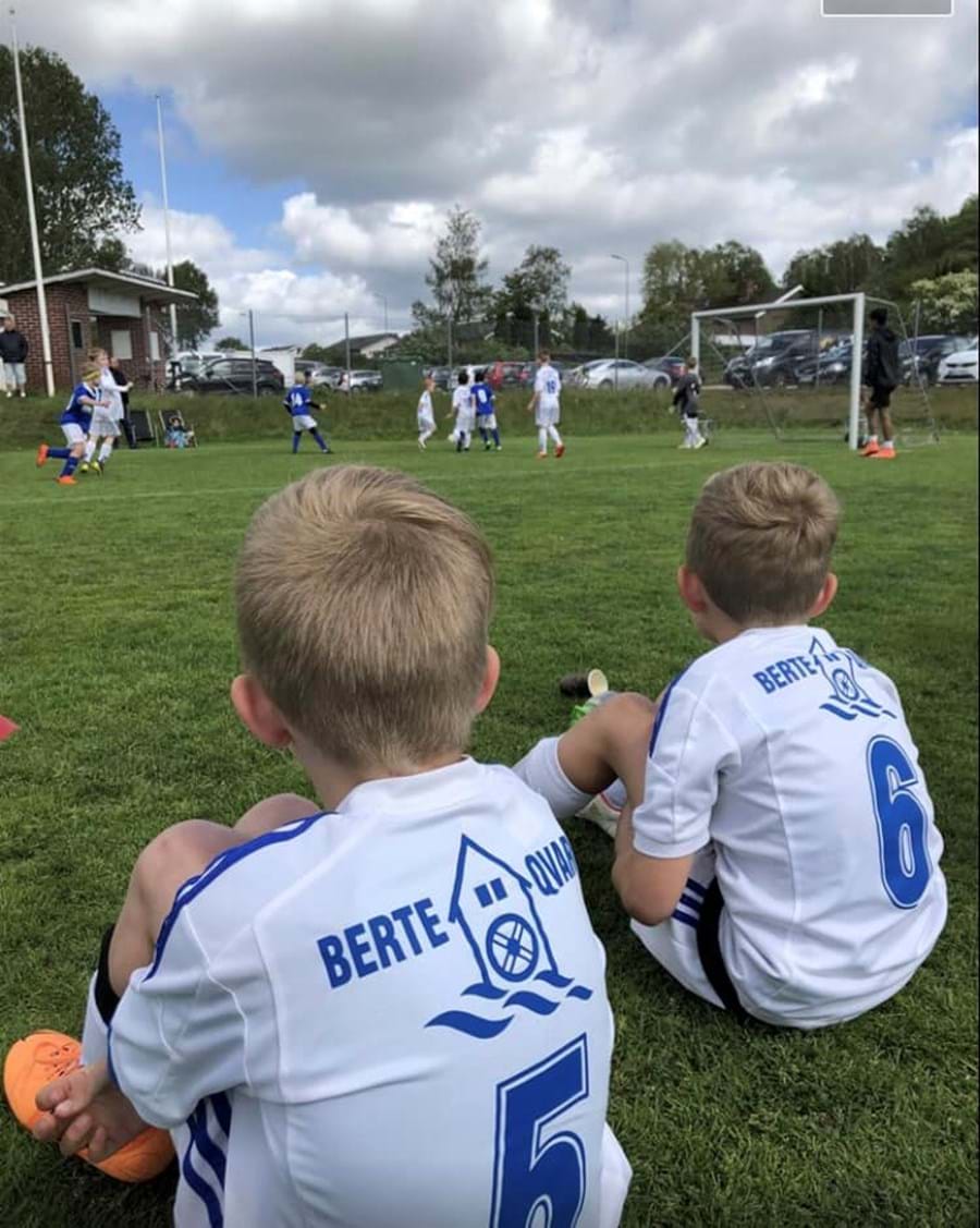 Två unga spelare i Slöinge GoIF sitter vid sidan av planen och tittar på matchen
