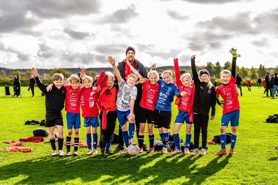 Barn i fotbollströjor och en ledare jublar på gräsplanen under Kycklingcupen